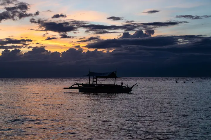 A bangka boat silhouetted on the water at sunset off Moalboal